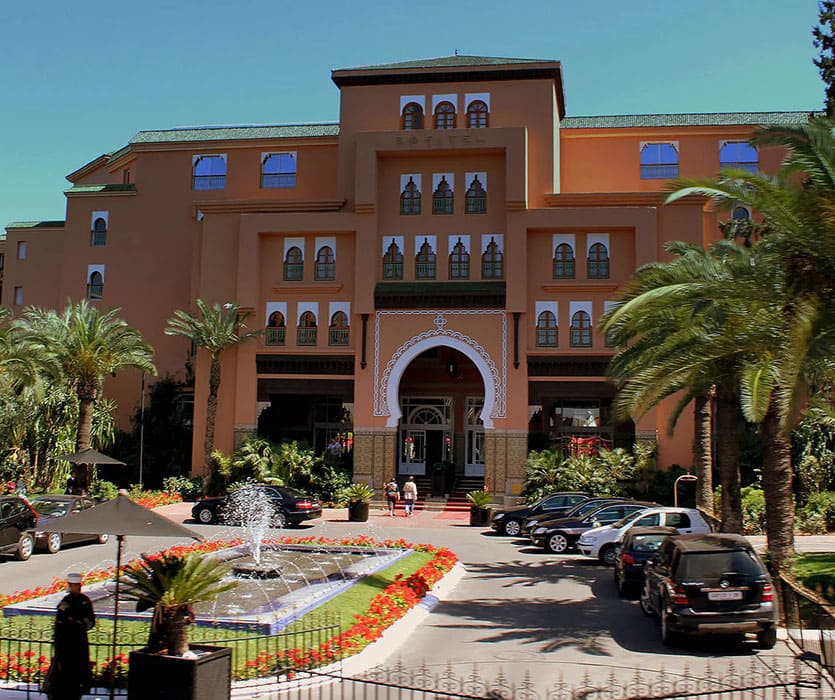 Hôtel marocain avec jardin, fontaine et palmiers devant l'entrée