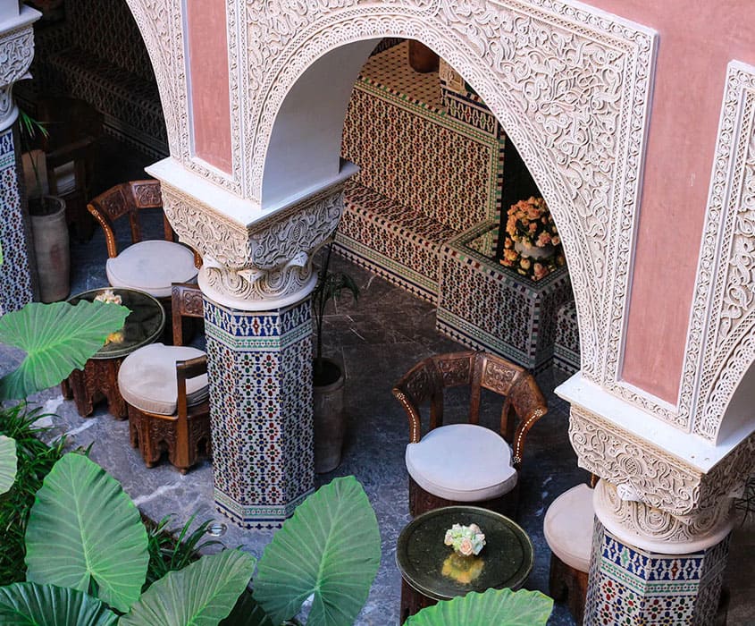 Patio marocain avec arches sculptées, mosaïques et mobilier en rotin