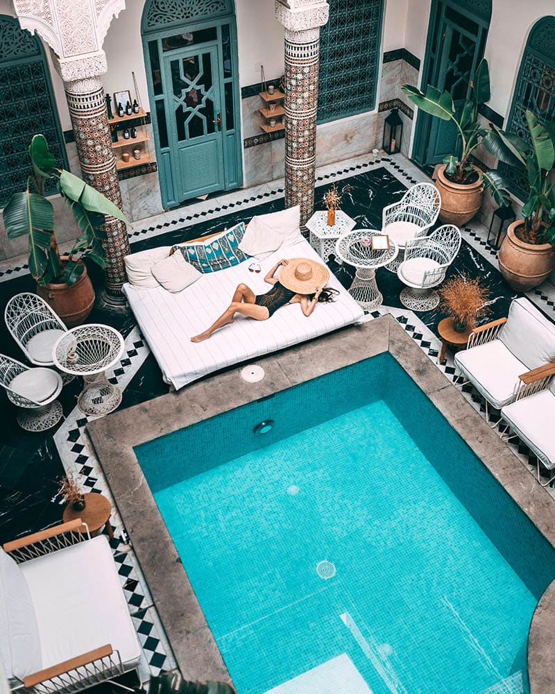 Cour intérieure avec piscine, femme allongée sur un lit, décor marocain