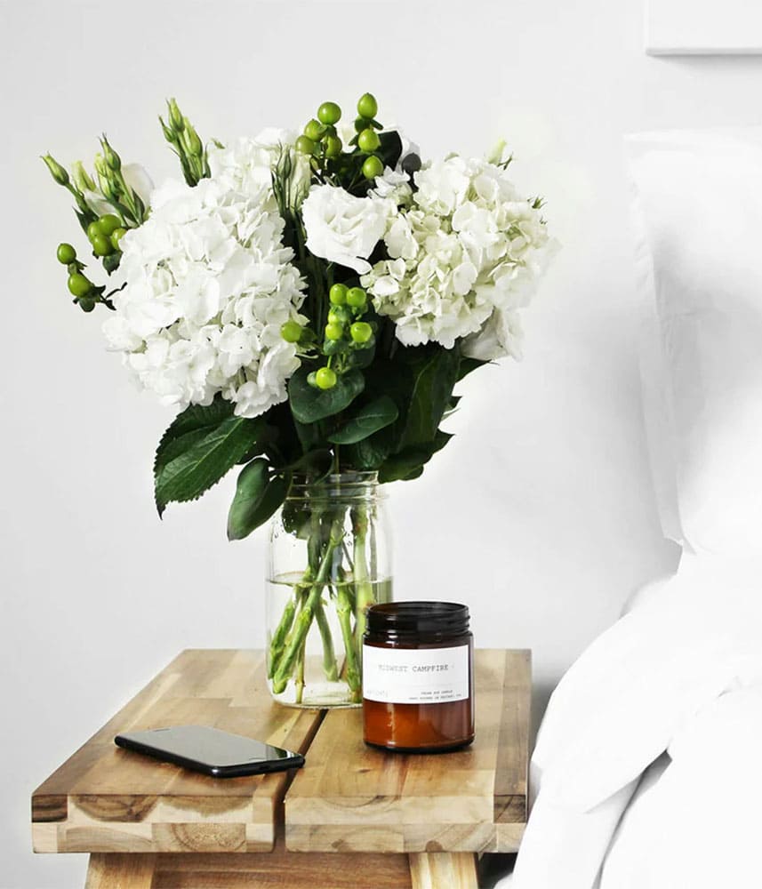 Fleurs blanches, bougie et téléphone sur table de nuit.