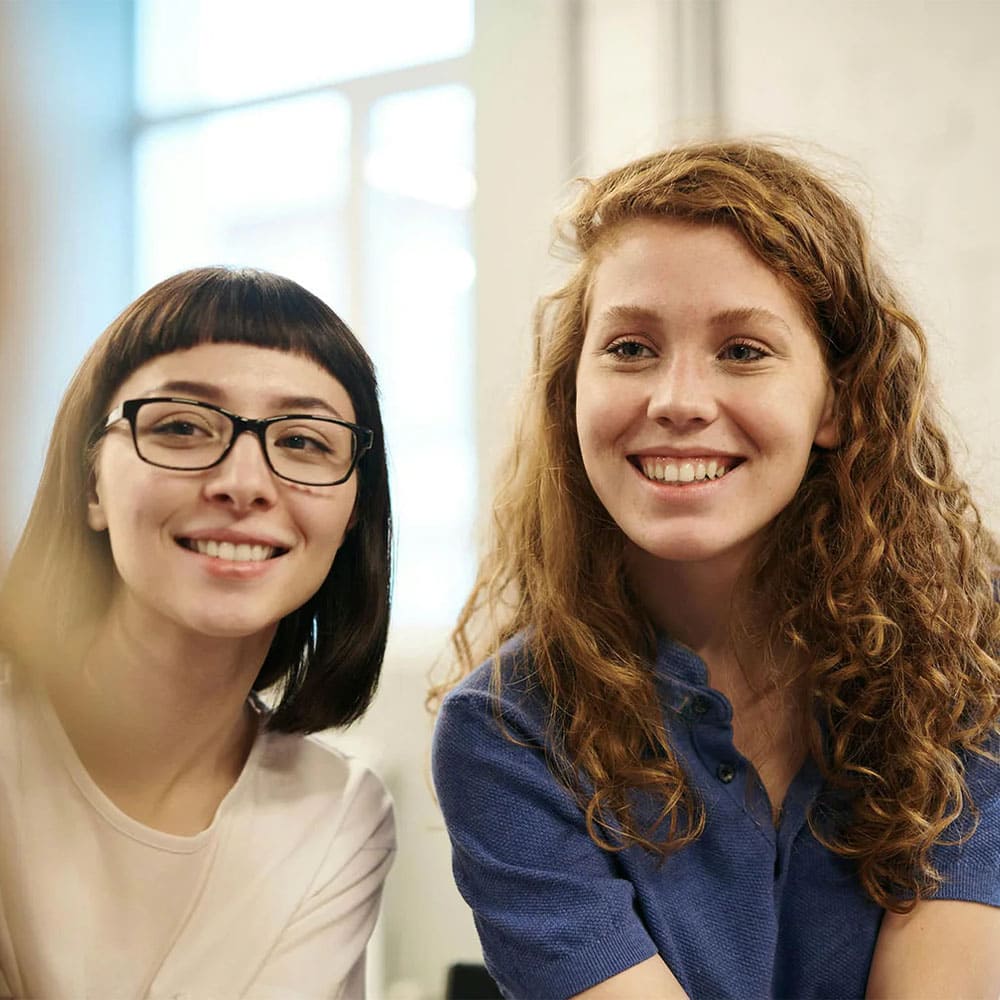 Deux femmes souriantes, l'une avec des lunettes, l'autre avec des cheveux bouclés